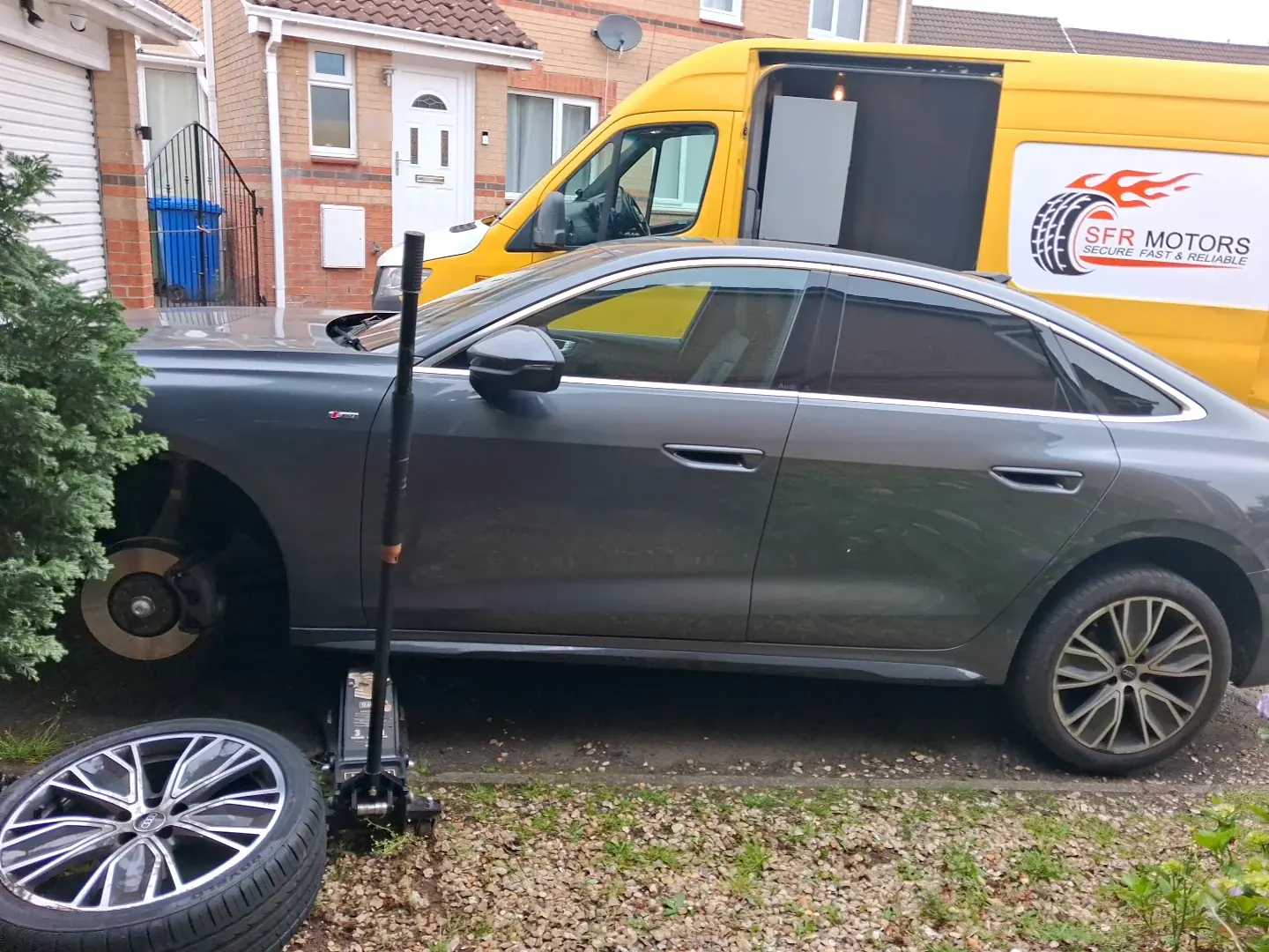 Grey Audi with a front wheel removed on a driveway, beside a yellow SFR Motors mobile tyre van
