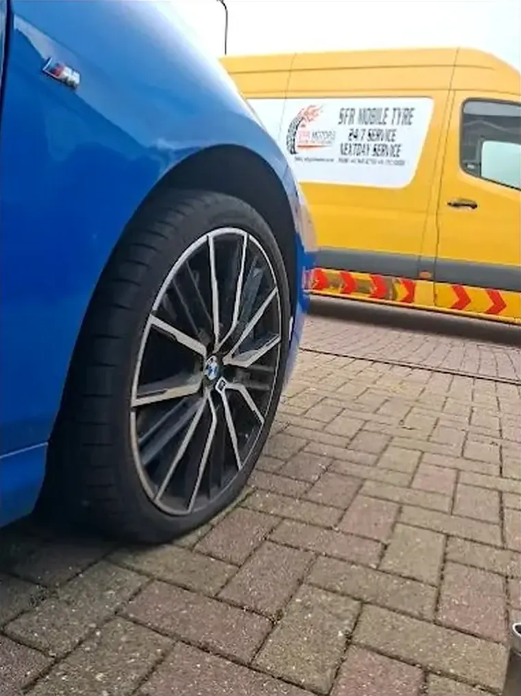 Alloy wheel on a blue car parked on block paving, with a yellow SFR Motors mobile tyre van in the background