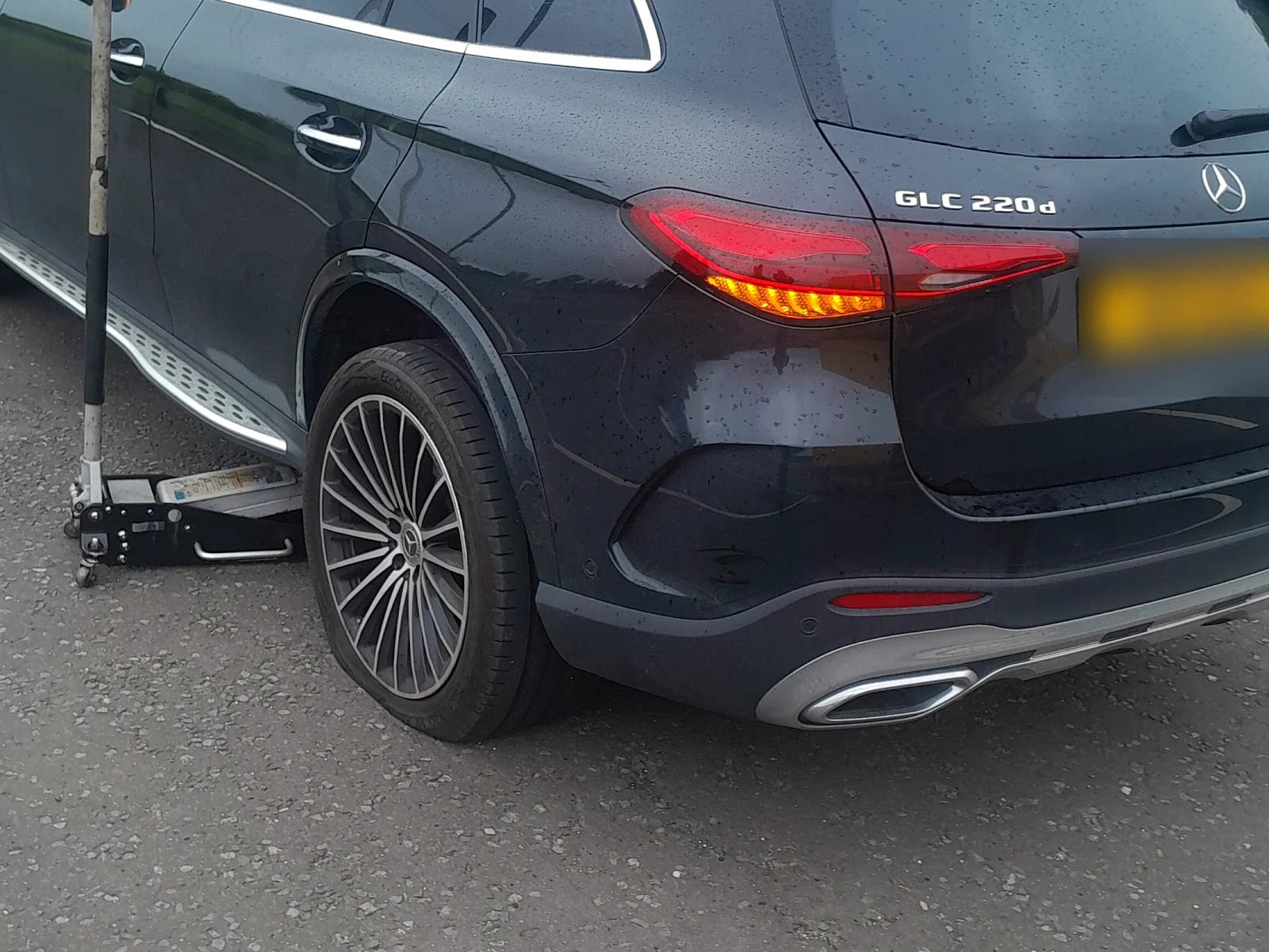 Rear wheel of a dark Mercedes SUV lifted on a trolley jack in a car park