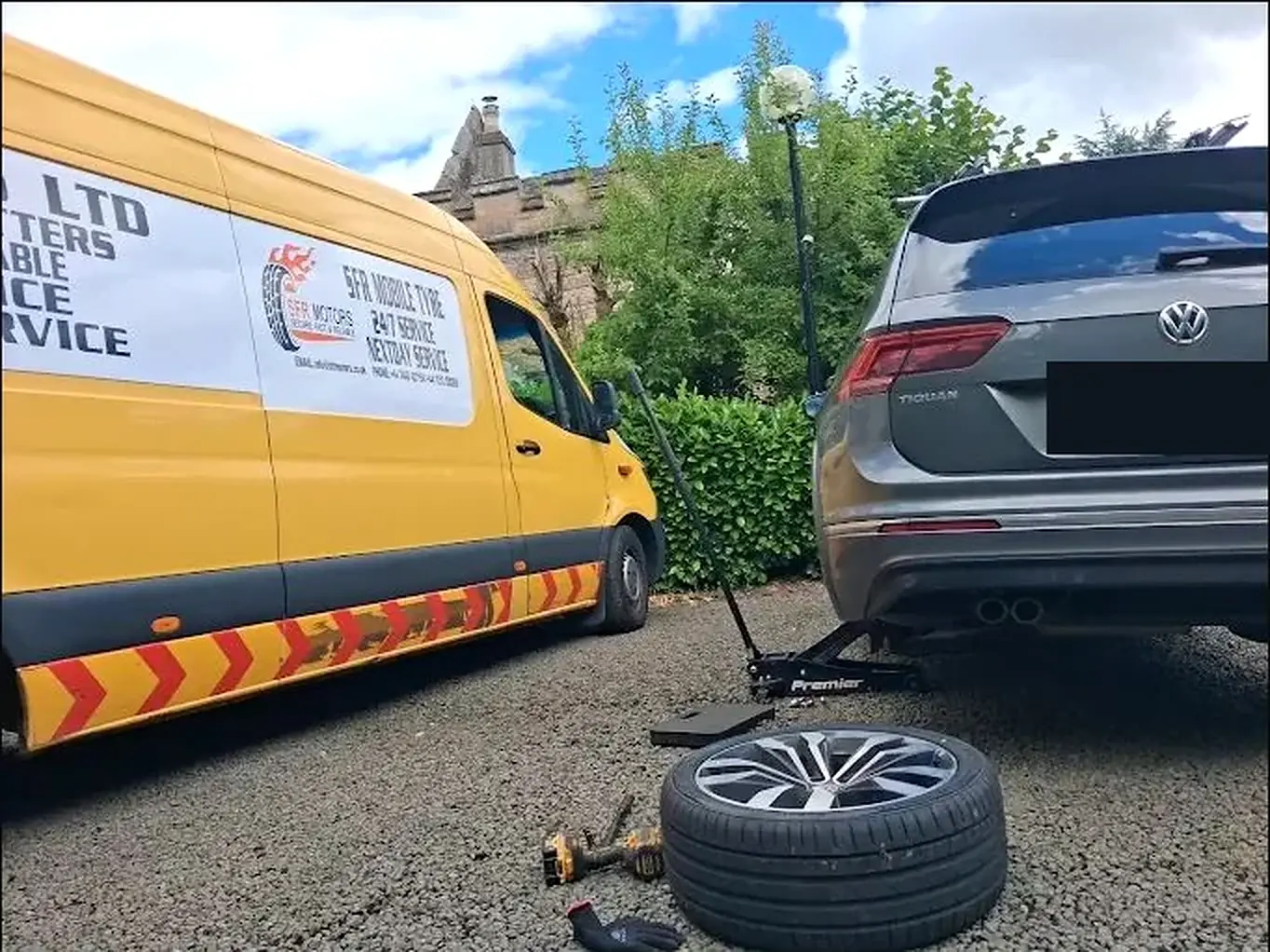 Grey Volkswagen SUV raised on a trolley jack with a wheel and impact wrench on the ground, beside a yellow SFR Motors mobile tyre van